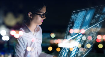 Businesswoman working at a futiristic digital interface screen with black background.