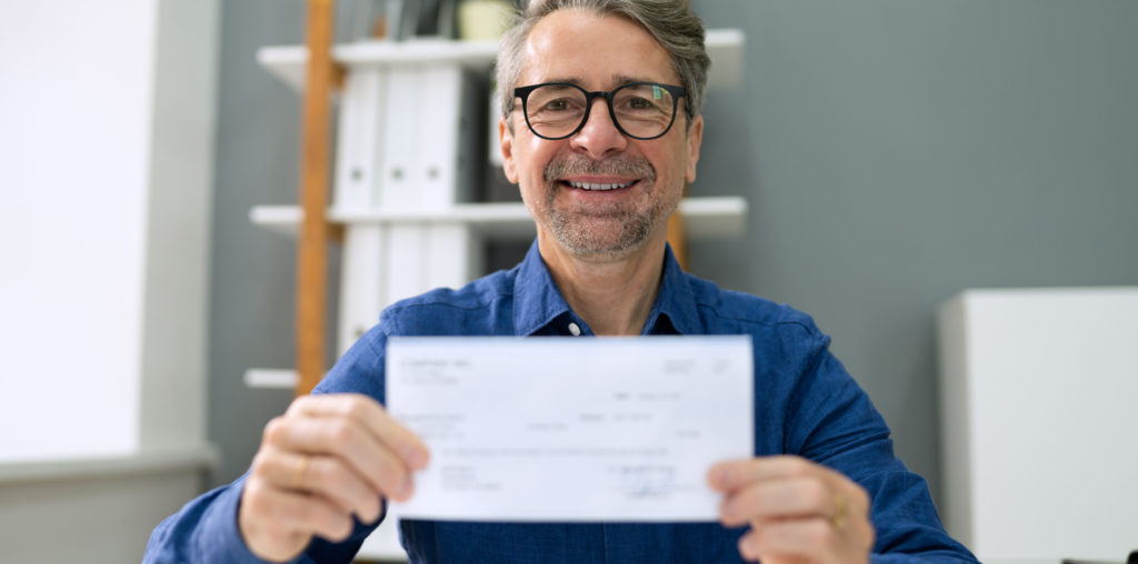 Businessman in blue shirt holding cheque with 2 hands.