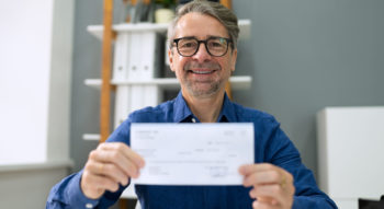 Businessman in blue shirt holding cheque with 2 hands.