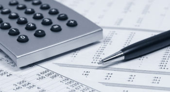 Desktop calculator and pen lying on top of financial reports.