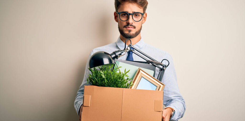 Young businessman holding cardboard box of belongings leaving office after being removed as a company director.