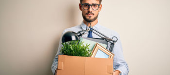 Young businessman holding cardboard box of belongings leaving office after being removed as a company director.