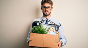 Young businessman holding cardboard box of belongings leaving office after being removed as a company director.