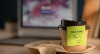 Close-up of a Welcome Back note on a takeaway coffee cup on an office desk. Concept of company coming back to life through administrative restoration.